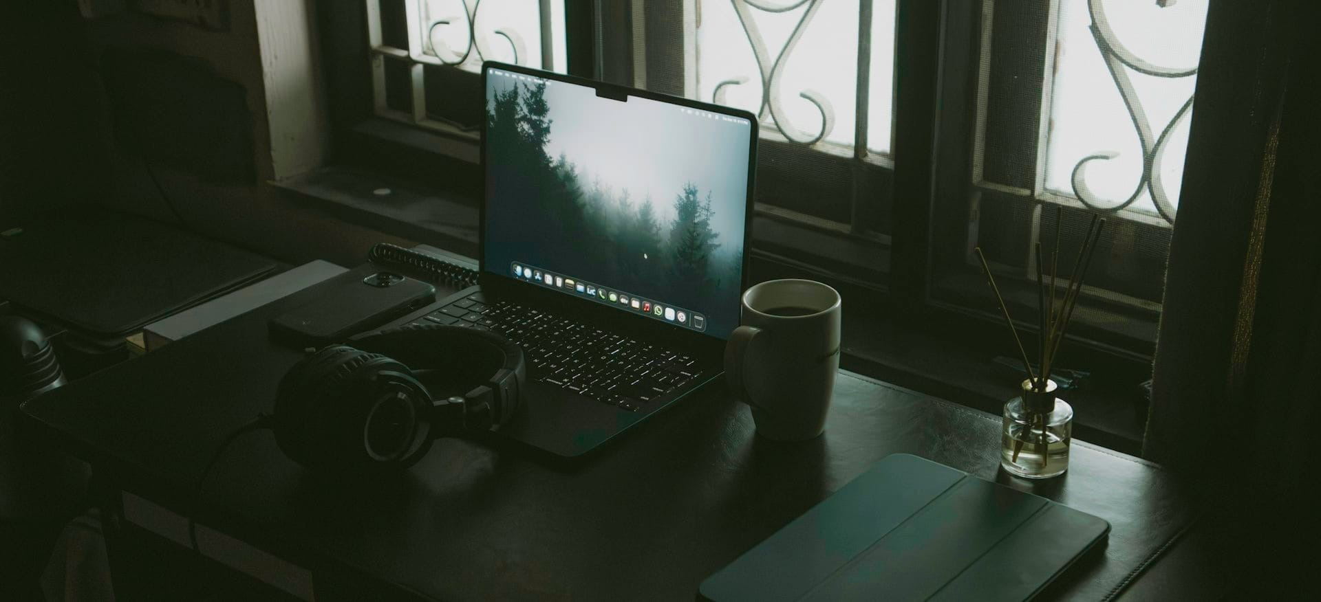 A laptop on a dark wooden desk by a window